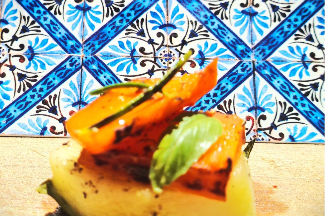 Symbol für Ernährungsberatung Gegrillter Kürbis auf einer weißen Unterlage, mit grünen Kräutern und buntem Fliesenmuster im Hintergrund.
